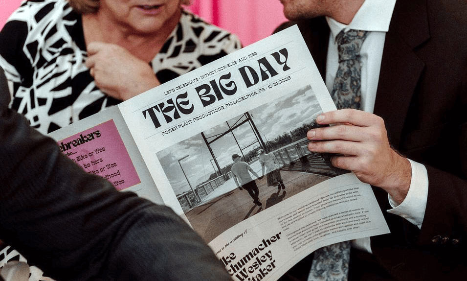 A tabloid-sized wedding newspaper titled The Big Day being read by two wedding guests.